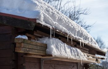 Snow-covered wooden roof with icicles hanging from the edge, set against a clear sky., 